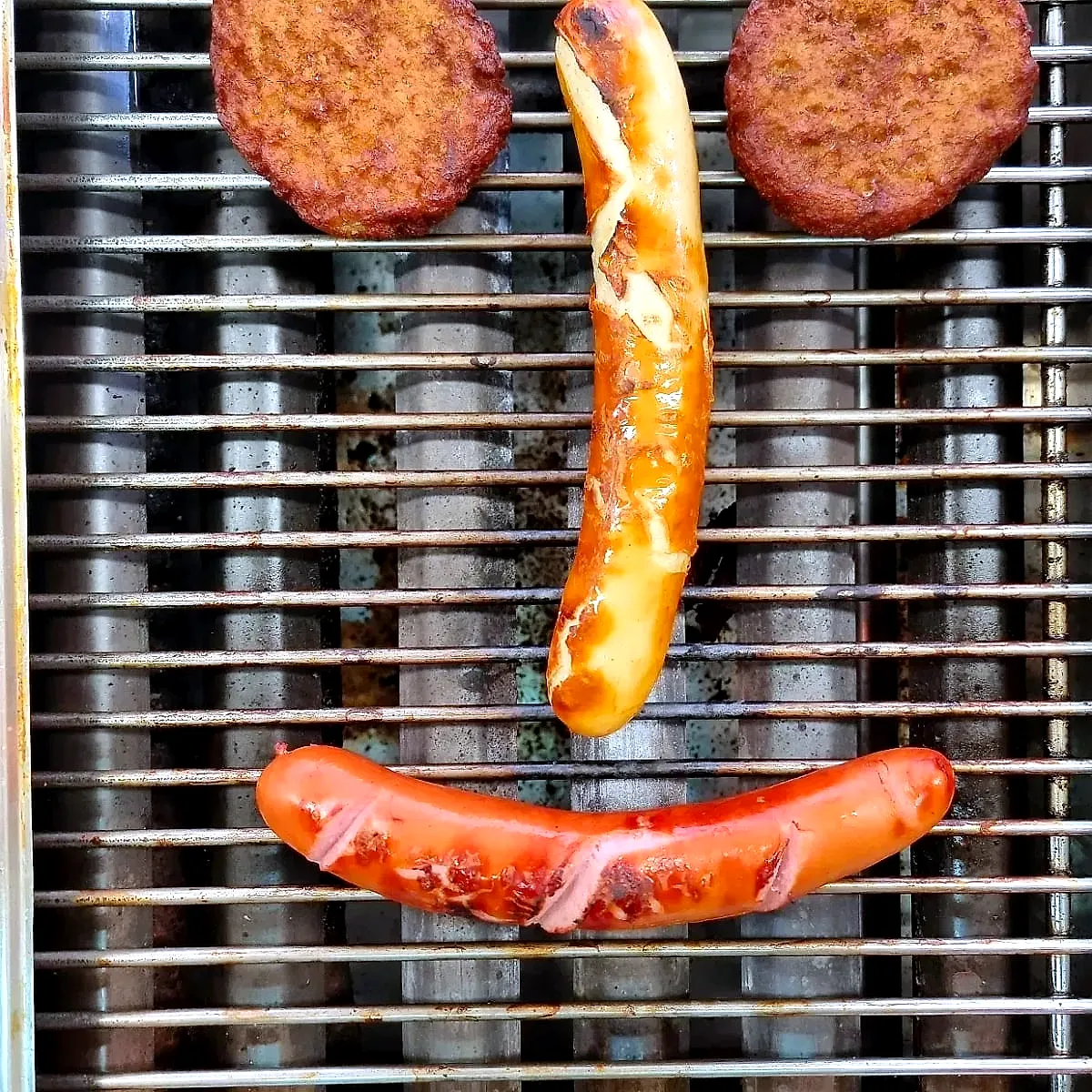 Zwei Frikadellen und zwei Würste auf dem Grill, als Gesicht gelegt